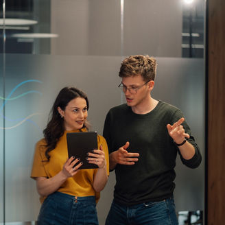 Two young business professionals are collaborating on a project, analyzing data on a tablet in a modern office environment
