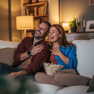 A husband and wife are watching a movie at night and eating popcorn in the living room.