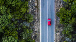 Arial view of te car running on road between the forest