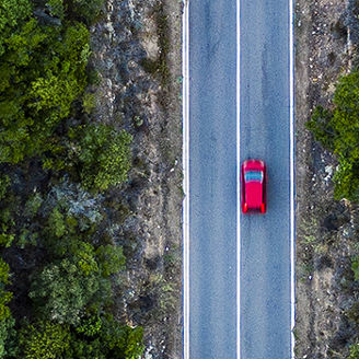 Arial view of te car running on road between the forest