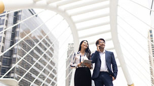 Asian business man talking on mobile phone and young beautiful woman working on digital tablet computer standing outside office building.