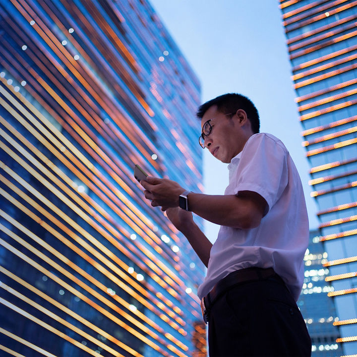 Young asian businessman wearing a white shirt and using a smartphone in front of corporate buildings