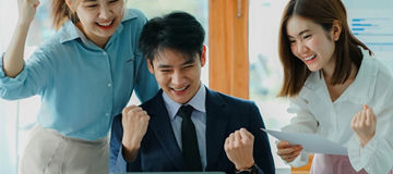 富有魅力的年轻商人和年轻的亚洲女性在办公桌前举手庆祝成功