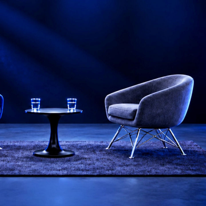 Zwei Sessel und ein kleiner runder Tisch mit zwei Wassergläsern in einem dunkelblauen Studio, links eine vertikale LED-Lichtleiste.