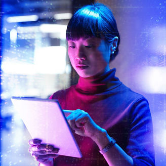 A woman olding and touching a tablet with both hands, illuminated by blue and pink lighting, with abstract digital light patterns and blurred structures in the background