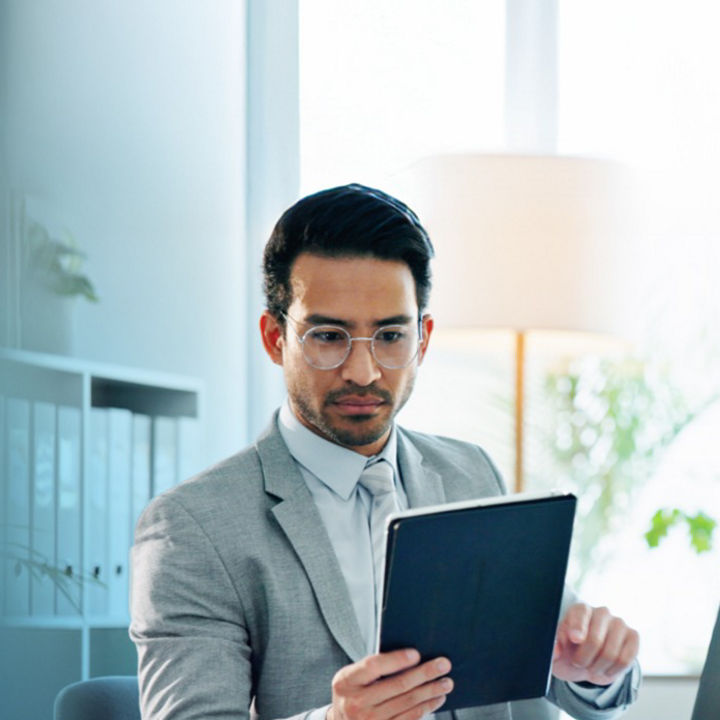 A person with glasses sat at an office table looking at a tablet