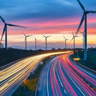 Autoestrada ao entardecer com trilhos de luz e aerogeradores eólicos sob um céu colorido.