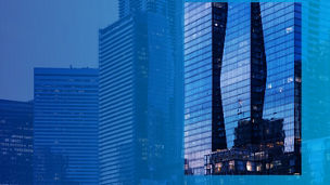 Städtische Skyline mit blauen Glasfassaden; zentrales Rechteck zeigt die Spiegelung zweier geschwungener Türme in der Fensterfront eines Hochhauses.