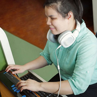 Blind person with headphones using computer with braille