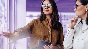 Mature business woman brainstorming with her colleague in an office. Female professionals discussing business ideas using sticky notes.; Shutterstock ID 2317231977; purchase_order: advisory assurance; job: anne rouschop; client: ai campagne