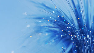 Abstrakte Aufnahme blauer Glasfaser‑Stränge mit leuchtenden Lichtpunkten vor hellem, blauem Hintergrund.