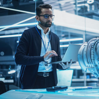 Young Industrial Engineer Working on a Futuristic Jet Engine, Standing with Laptop Computer in Scientific Technology Lab. Scientist Developing a New Electric Motor in a Research Facility.