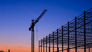 Silhouette of large industrial building structure with pile driver and many precast concrete piles in construction area against colorful twilight sky background