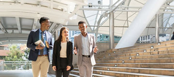 Three business people talking whilst walking outside next to steps