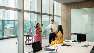 Three Indian employees talking during break in the meeting room of a modern business building