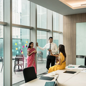 Three Indian employees talking during break in the meeting room of a modern business building