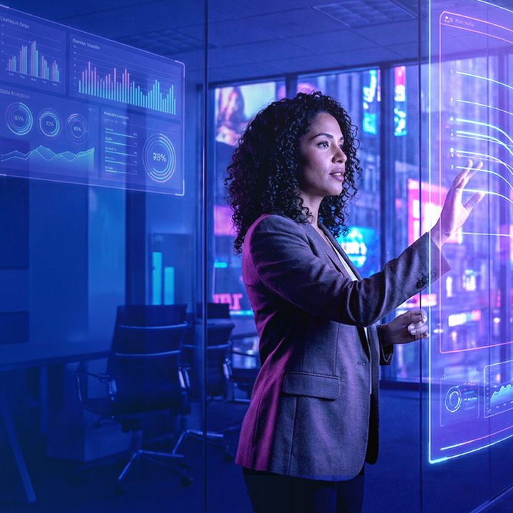A woman in a business suit interacts with a transparent digital display showing various data charts and graphs