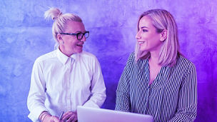 Two collegues laughing, with laptop and notebook in hand
