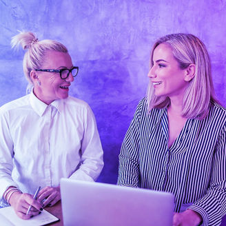 Two collegues laughing, with laptop and notebook in hand