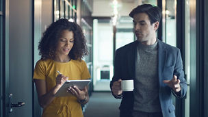 Business woman using tablet talking to man with coffee in a hallway