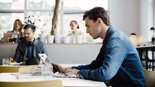 Side view of young businessman using laptop while sitting at desk in coworking space