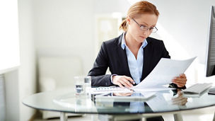 Young businesswoman sitting at workplace and reading paper in office