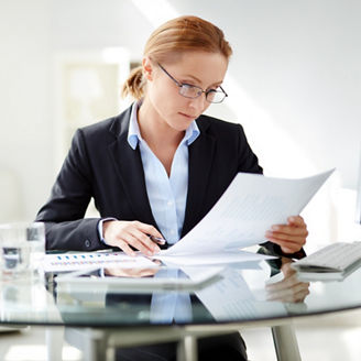 Young businesswoman sitting at workplace and reading paper in office