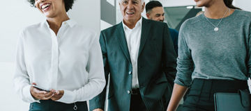 Diverse group of business people walking through office corridor.  Team of corporate professionals walking and talking in modern office hallway.