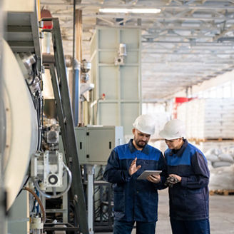 Two young contemporary workers of modern plant discussing online technical data or sketches of details for industrial machines in workshop