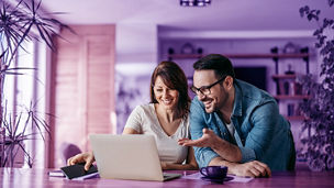 Portrait of a smiling couple looking at laptop together at cozy home office.