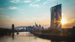 city-view-with-tall-building-in-focus-at-riverbank-sun-blue-sky-and-bridge