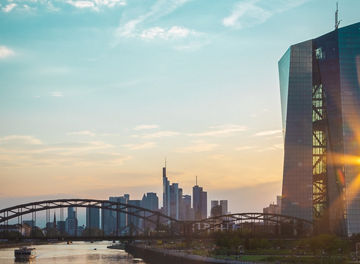 city-view-with-tall-building-in-focus-at-riverbank-sun-blue-sky-and-bridge