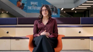Person seated on an orange chair in a modern office, facing forward, with signage and stairs in the background