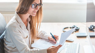 Accountant writing on paper at home office desk - Young business woman doing remote work, reading and writing - Home office or small company start up in London