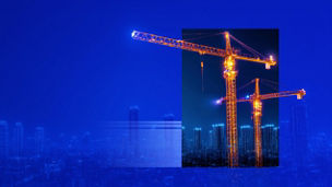 Construction cranes lit up over a city skyline at night banner