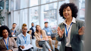 Corporate training workshop with a presenter and attendees in a conference room.