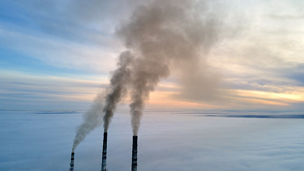 Aerial view of coal power plant high pipes with black smoke moving up polluting atmosphere at sunset.