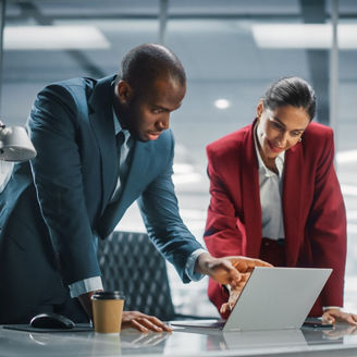 People looking at a laptop whilst leaning on a desk in an office