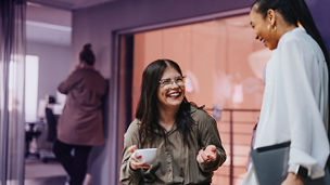 Happy female business professional holding coffee cup and discussing with colleague in office