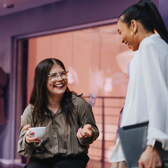 Happy female business professional holding coffee cup and discussing with colleague in office