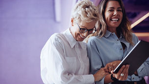 Two business women celebrate their company's success with laughter after reading a positive business report on a digital tablet. Female executives working together in an office.; Shutterstock ID 2350375695; purchase_order: marketing advisory assurance; job: Anne; client: AI campagne