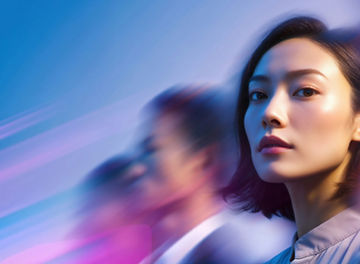 A professional woman in the foreground looks confidently at the camera while blurred figures move behind her against a blue and purple background.