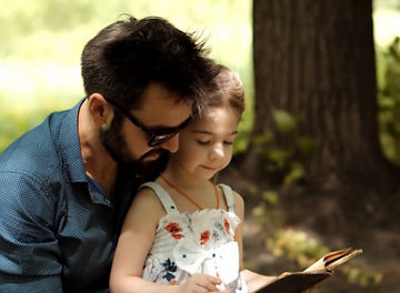 Dad and daughter in park reading a book
