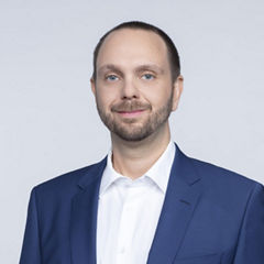 Porträt von Daniel Kroiss vor einer hellgrauen Wand