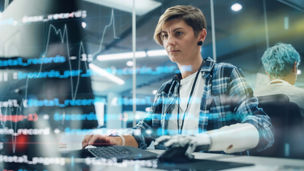 Shot with Visualisation of Running Computer Code on Foreground. Portrait of Motivated Woman with Disability Using Prosthetic Arm to Work on Computer in Body Positive Office. Myoelectric Bionic Hand