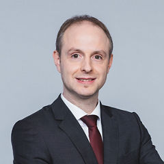 Porträt von Dominik Lasser vor einer hellgrauen Wand