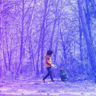 Black child picking up a plastic bottle from the forest to recycle