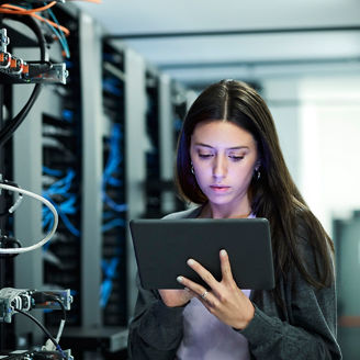 Female technician using digital tablet in server room. IT professional is standing at workplace. She is in casuals.