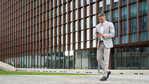 Rich middle aged businessman using cellphone walking on city street, busy older business man leader investor, mature male executive in suit holding mobile phone going near office building, full body.