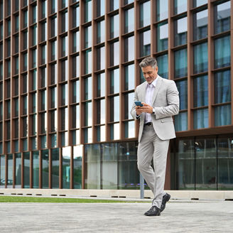 Rich middle aged businessman using cellphone walking on city street, busy older business man leader investor, mature male executive in suit holding mobile phone going near office building, full body.